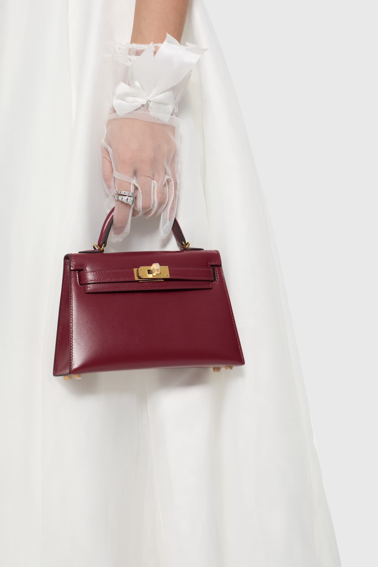 C4856 The white veil reflects purity; Kelly19 embodies Hermès’ red accents and perfection. The mini-sized design does not restrict the fluffy skirt edge; the intense red leather contrasts with the white satin. The H-button pairs well with the diamond deco — image 8