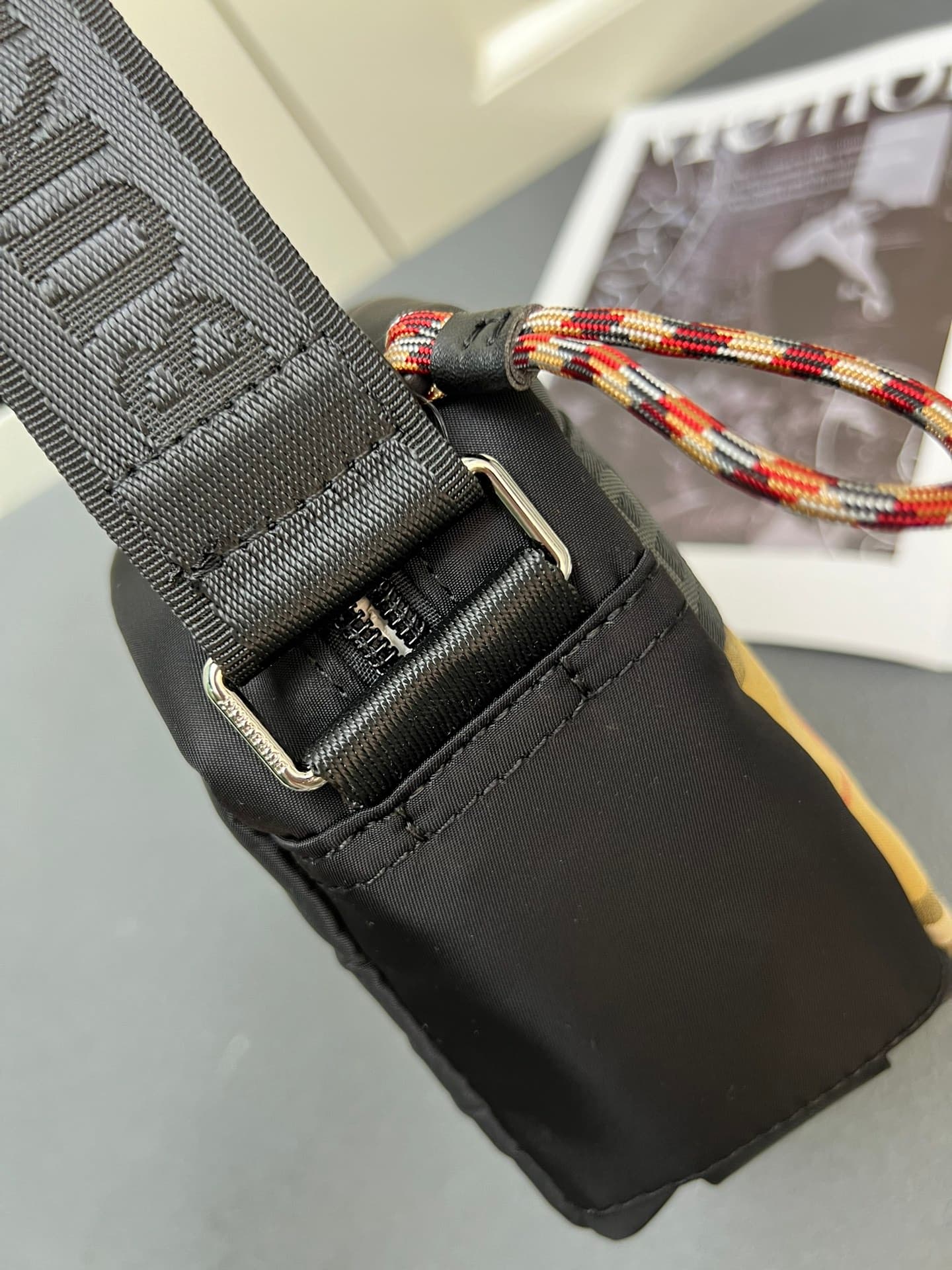 C36 [Brand B] 200: A vibrant decorative bag with a plaid pattern in the “Bur” style. It features a strap with a brand logo embroidered on it. There is an adjustable diagonal shoulder strap, as well as a zipper pocket. The 1 external pocket is opened using — image 6